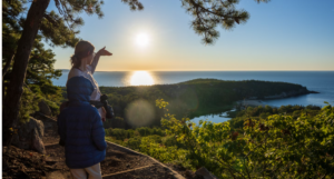 WOMAN WITH HER CHILD AT ACADIA NATIONAL PARK LOOKING OUT AT THE BEAUTIFUL SKY AND OCEANVIEW