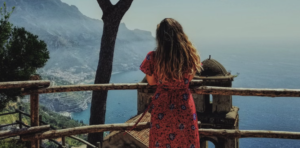 WOMAN IN PEACH PRINT DRESS STANDING ON DECK LOOKING OUT AT THE BEAUTIFUL OCEAN VIEW