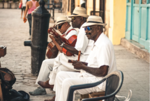 A LOCAL MALE BAND DRESSED IN WHITE TOP AND WHITE PANTS WEARING WHITE HAT WITH A THINK BLACK CIRCUMFERENCE PLAY FOR CUBAN VACATION TRAVELERS