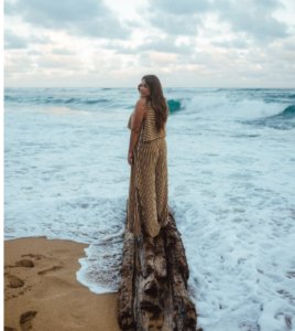 WOMAN WITH LONG WAIST-LENGTH HAIR STANDING ON LANDING NEAR OCEANSIDE IN HAWAII IN A LOMG BEIGE MAXIE DRESS