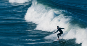 EXPERT SURFER IN A BLACK WET SUIT DOING HIS THING  AS A SAN DIEGO TRAVELER