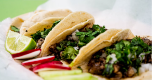 PLATE WITH THREE DELICIOUS TACOS   IN A FLOUR TORILLA AND SLICED RADISHES AND ONIONS ON THE SIDE