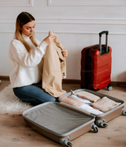 YOUNG LADY SORTING ITEMS TO PUT IN HER LUGGAGE TO TAKE ON HER UPCOMING CRUISE. WEARING A WHILE LONGSLEEVED TOP AND BLUE GENES.