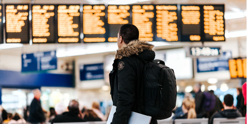 MAN IN BLACK JACK WITH FIR COLLAR CARRYING BACKPACK AT AIRPORT