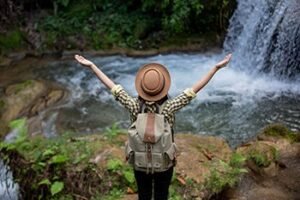 TOIRIST STANDING ON PLATFORM AT A NATIONAL PART=K WEARING STRAW HATM BACKPACJ WITH ARMS REACHING OUT TO THR WORLD